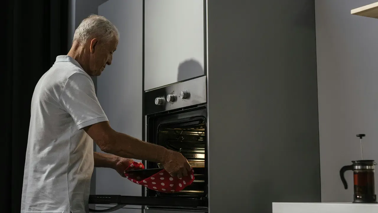 En la foto: Señor de edad cocinando en horno de cocina