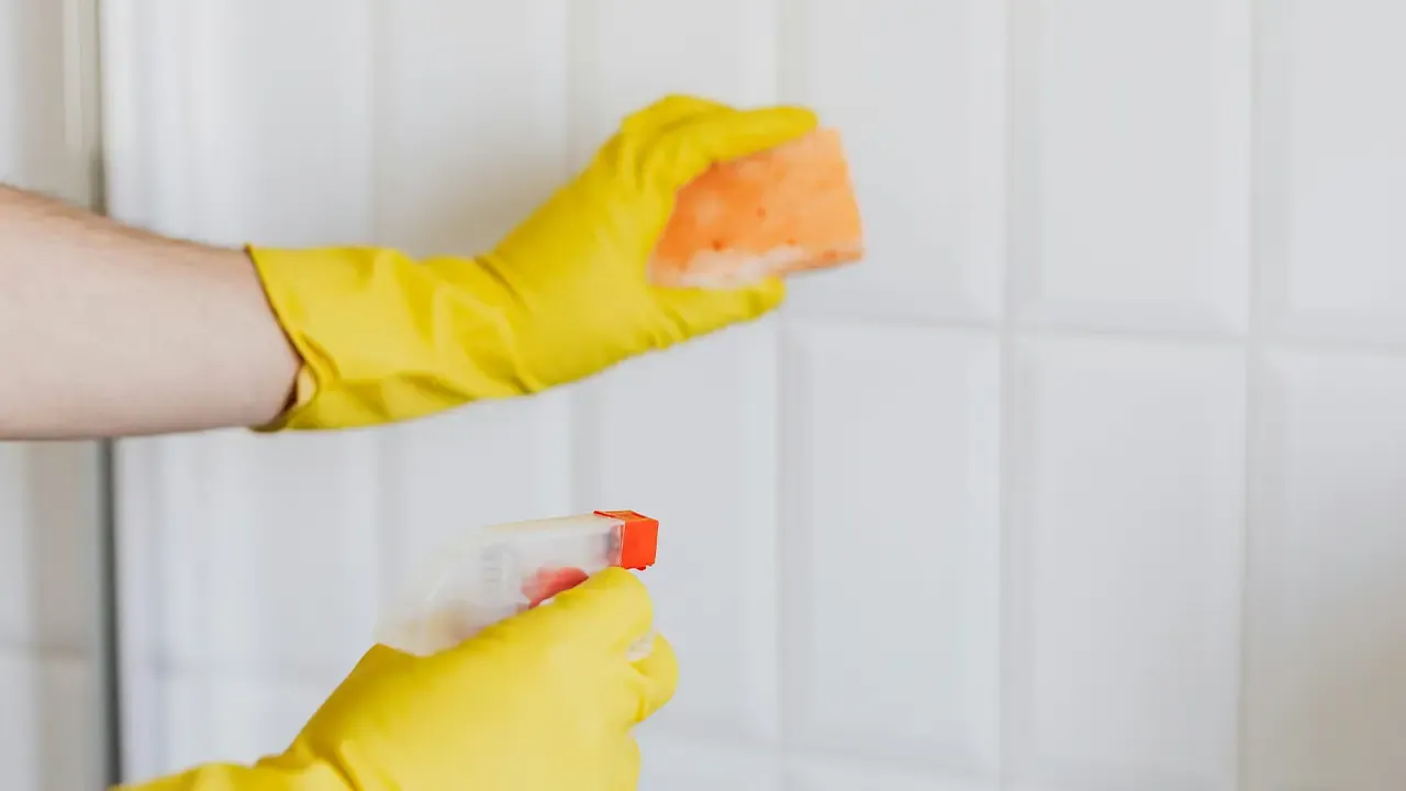 En la foto: Manos haciendo aseo en un baño con guantes amarillos
