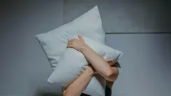 En la foto: Persona cubriéndose el rostro con almohadas
