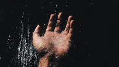 En la foto: Mano de un hombre recibiendo el agua sobre un fondo oscuro.